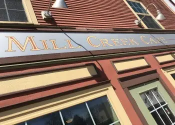 A close up of a restaurant sign for Mill Creek Cafe on the red and yellow accented building.