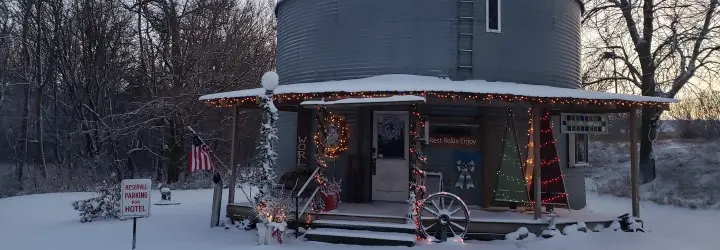 A grain bin with a wooden porch and Christmas lights surrounded by snow.