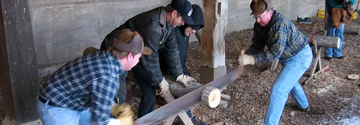 Three men compete in a log sawing competition.