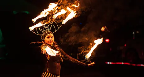 A fire dancer performs in the dark night with flames crowning her head and hands.
