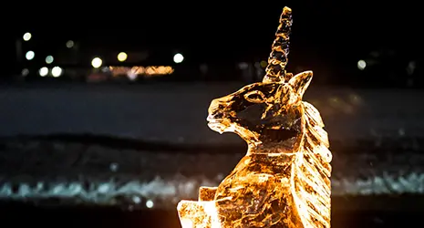 A unicorn ice sculpture is illuminated by a golden light in the pitch black night.