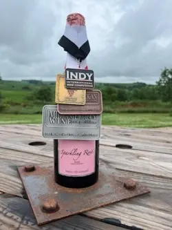 A bottle of wine is donned in several award medals sits on a wooden table.