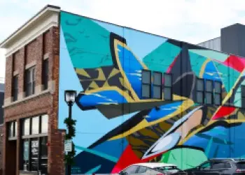 A brick building features a colorful, abstract mural on one side featuring blues, greens, yellows and reds.