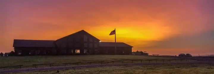 A large building with a bright orange, pink and yellow sunset behind it.