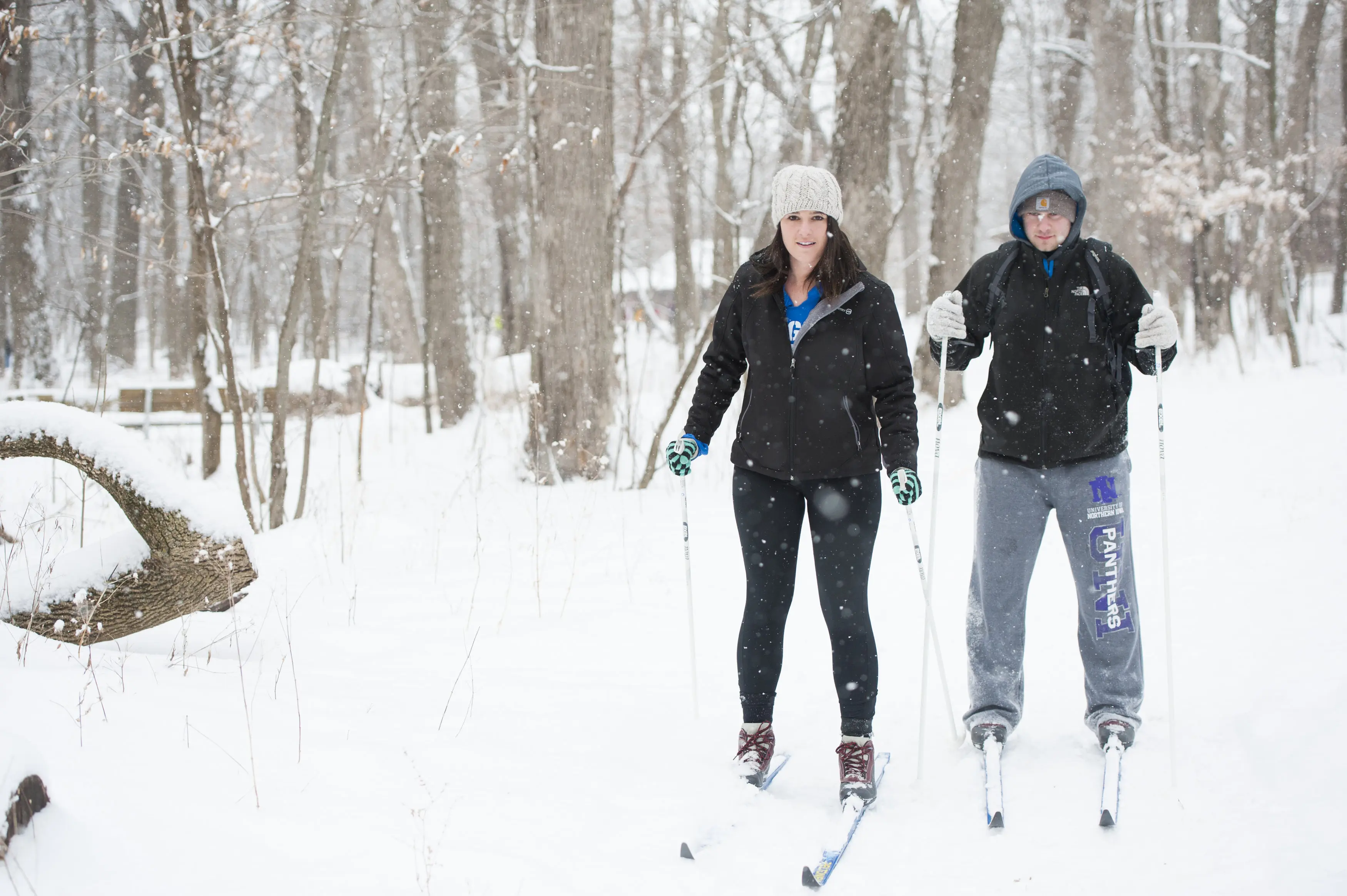A young white couple cross-country skis through a forest.
