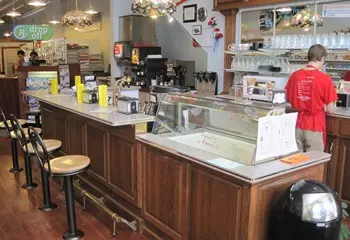 A red-shirted employee stands behind an old soda fountain counter.