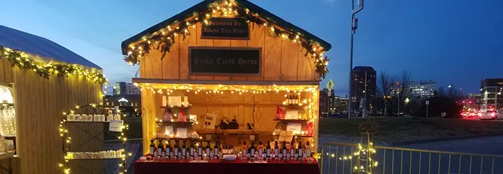 A small wooden hut hosting a craft vendor is illuminated by holiday lights.