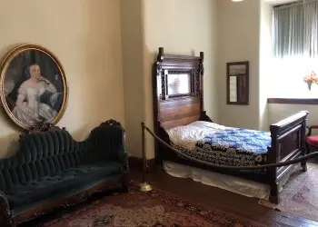 A historic bedroom features an old wooden bed and frame, sofa and portrait.
