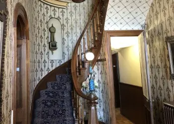 A spiral staircase leads to an upper level from a heavily wallpapered hallway.
