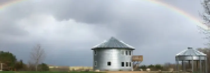 A grain bin with an upper level wooden deck sits beneath a full rainbow.