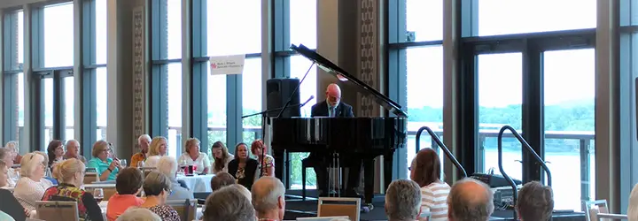 A man sits behind a grand piano on an elevated stage before a crowd. 