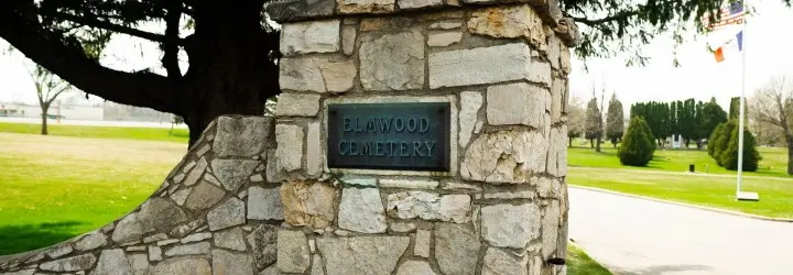 An old stone gate with a rusting sign reading "Elmwood Cemetery."