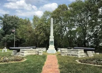 A tall white pillar is surrounded by four historic war cannons.