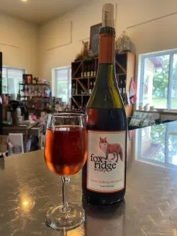 A glass of pink wine sits next to it's accompanying bottle inside a store.