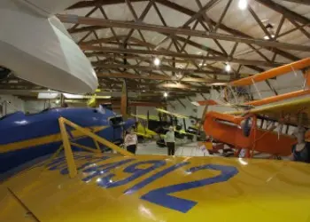 A collection of historic airplanes fill a large, wooden-beamed shed.