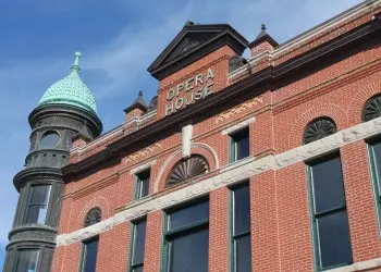Looking up at a historic red brick opera house with a green-roofed turret. 