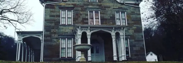 A creepy brick home features a small covered front porch and three upper story windows.