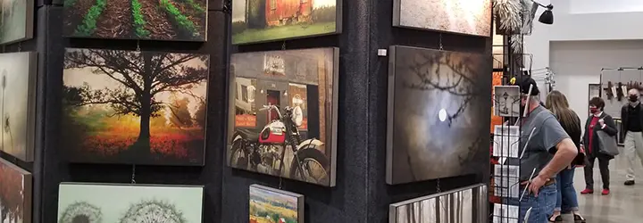 A collection of paintings on display as shoppers browse art stands behind them.