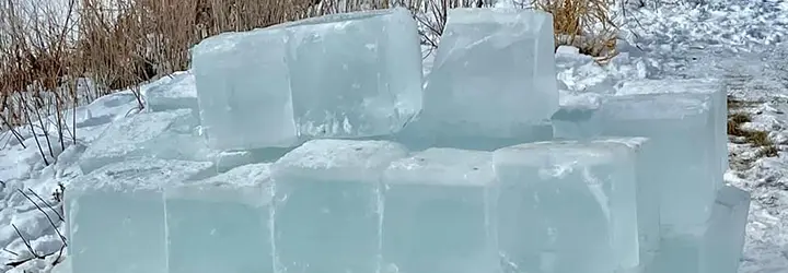 A stack of ice blocks cut from the local river sit on the snow covered ground.