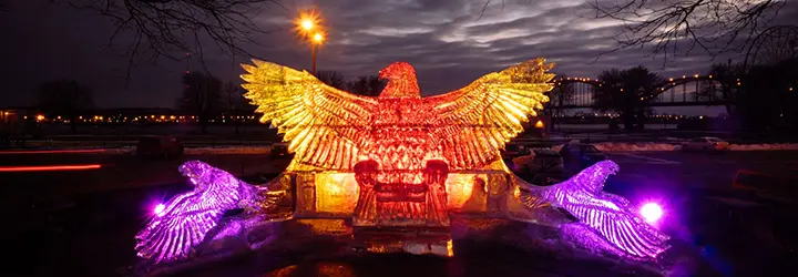 An ice sculpture of a bird with its wings spread is illuminated by orange-red lights.
