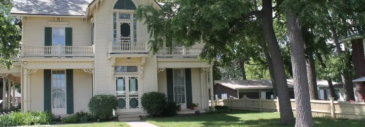 A sidewalk leads up to the front steps of a historic yellow home's double-doored entry.