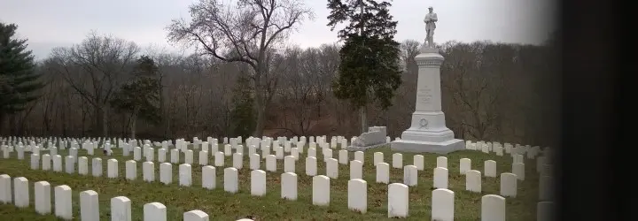 A group of small, white arched tombstones surround a white memorial pillar.