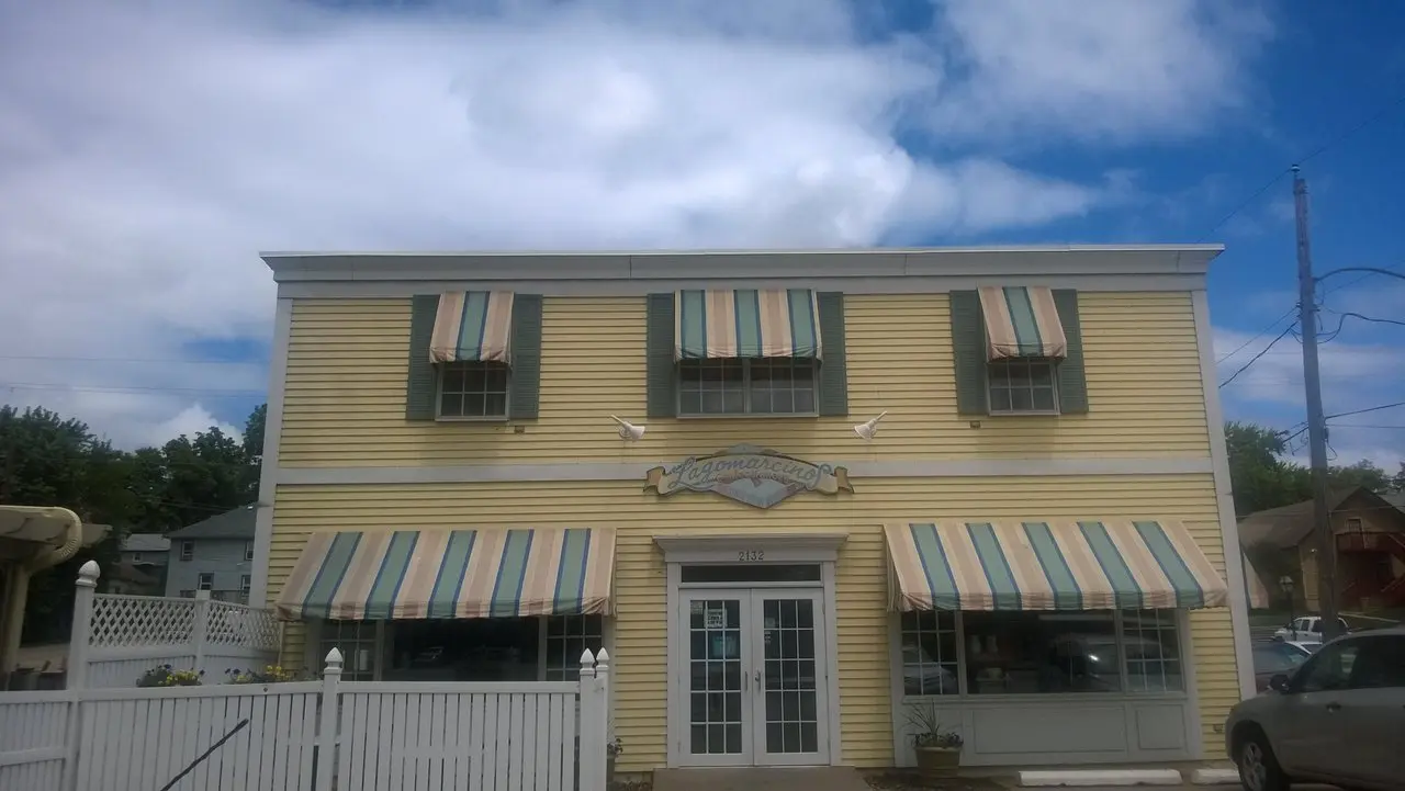 A yellow-sided building with yellow and green striped awnings over two lower windows on either side of the door and three upper windows.