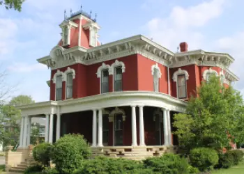 A historic red brick home features a wraparound porch and an ornate white trim.