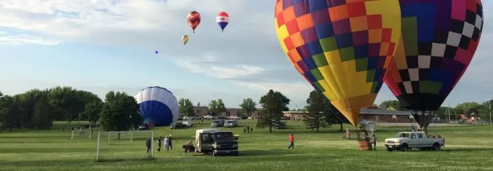 Two hot air balloons inflate on the ground while several more fly above. 