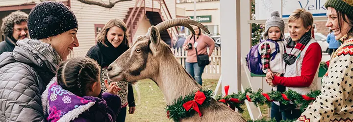 A group of women and children interact with a goat at a holiday event.