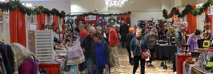 A crowd wanders a hallway filled with craft vendors and decorated with holiday wreaths.