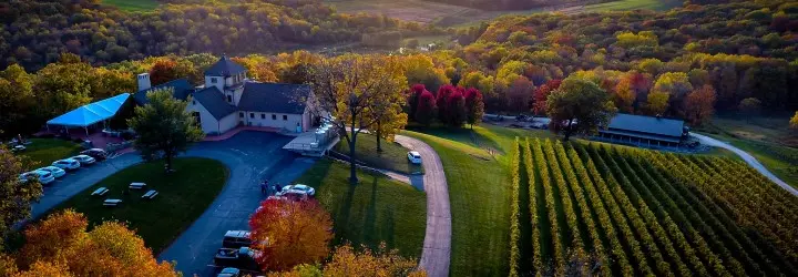 A large building and vineyard surrounded by fall-colored trees and rolling hills.