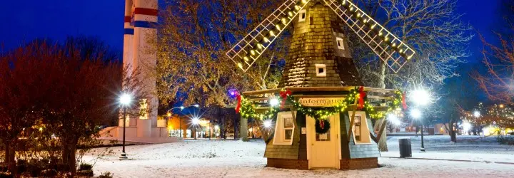 A historic windmill is donned in holiday lights and breaths in a snow-covered town park.