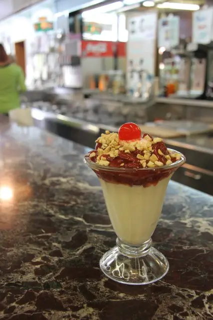 A chocolate and cherry topped sundae sits on a black marble counter.