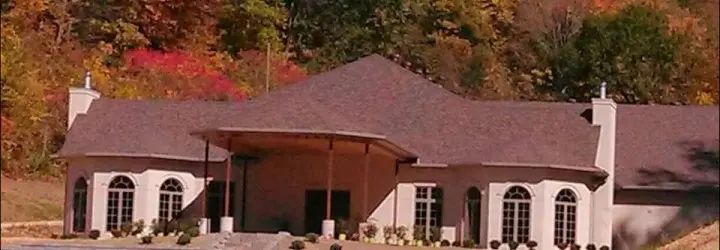 A large building and vineyard surrounded by fall-colored trees.