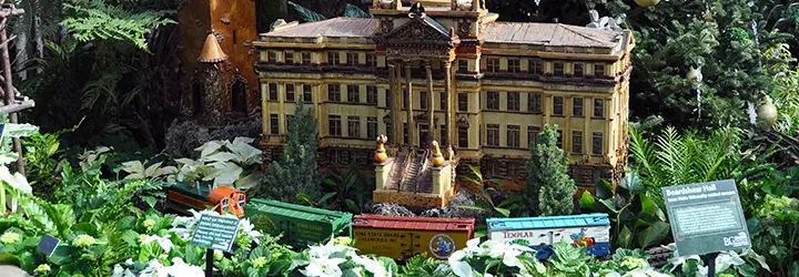 A miniature train passes in front of a miniature grand university building surrounded by green foliage.