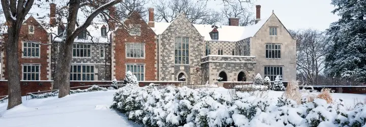 An extravagant home constructed with various brick colors looms over a snow-covered lawn.