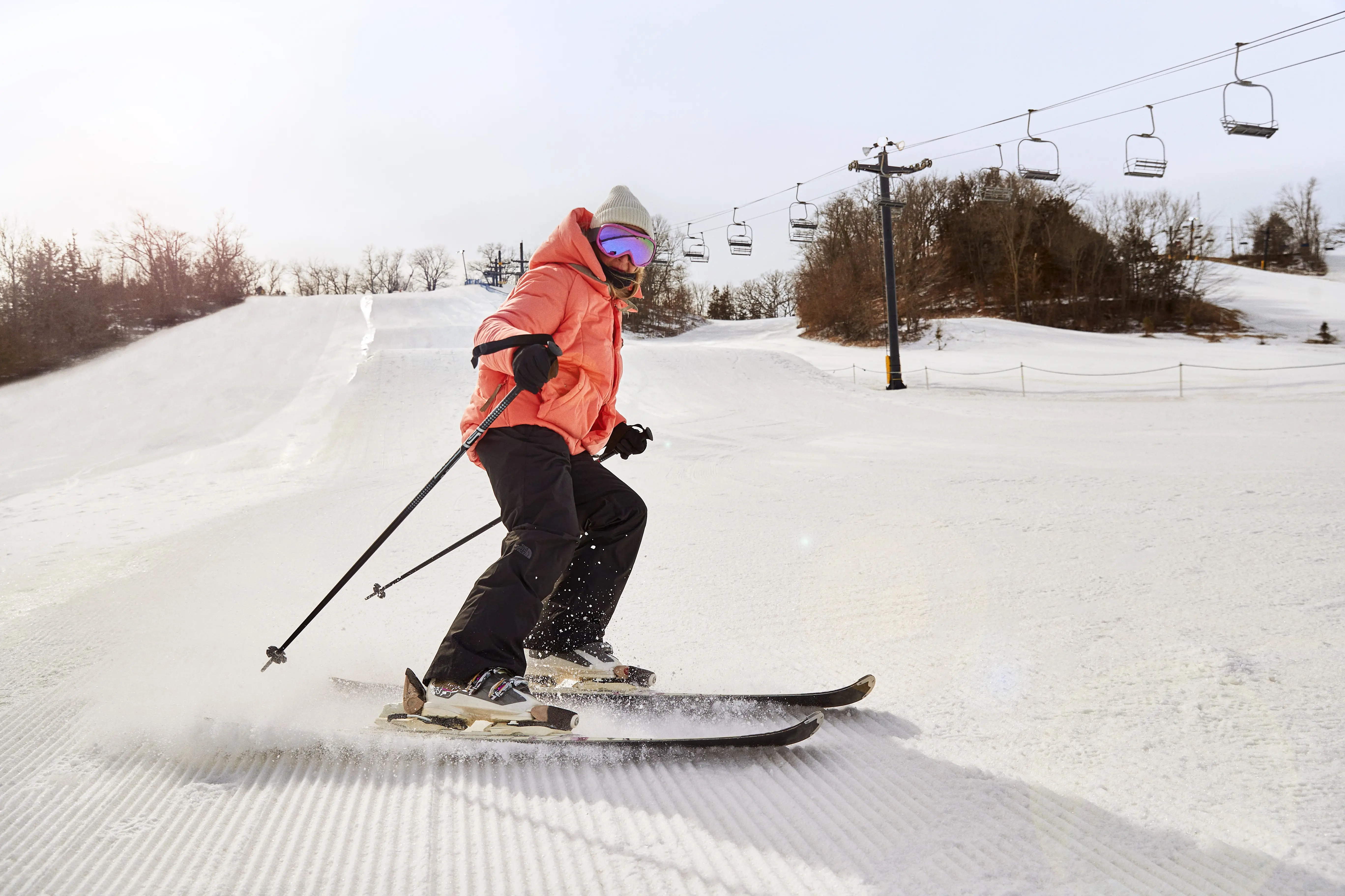 A skier in an orange coat skids to a stop at the bottom of a slope.