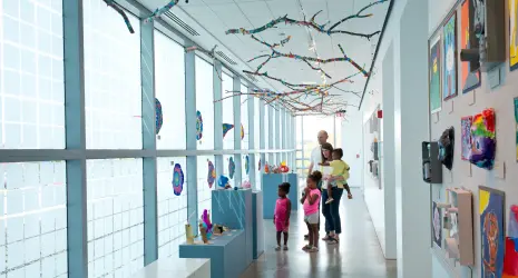 A black family explores a brightly lit hallway filled with wall art and ceiling pieces.