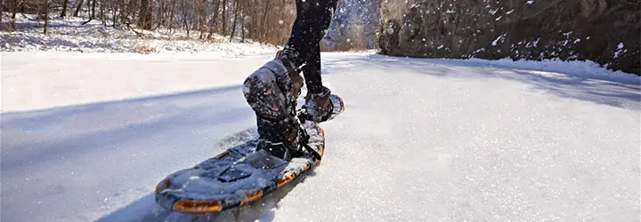 A close up of a snowshoe kicking up snow on a tree and bluff-lined trail.