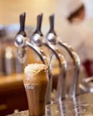  Three soda fountain handles stand behind a whipped-cream-topped root beer float.