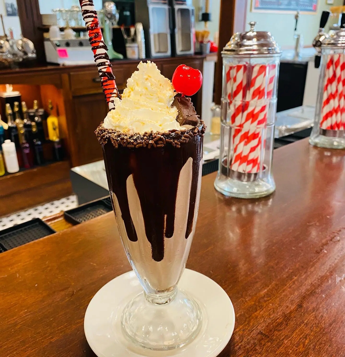 A gourmet sundae topped with whipped cream, chocolate and a cherry sits on a wooden counter.