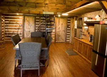 A dining room/kitchen with wooden floors, cabinets and wood paneled walls.