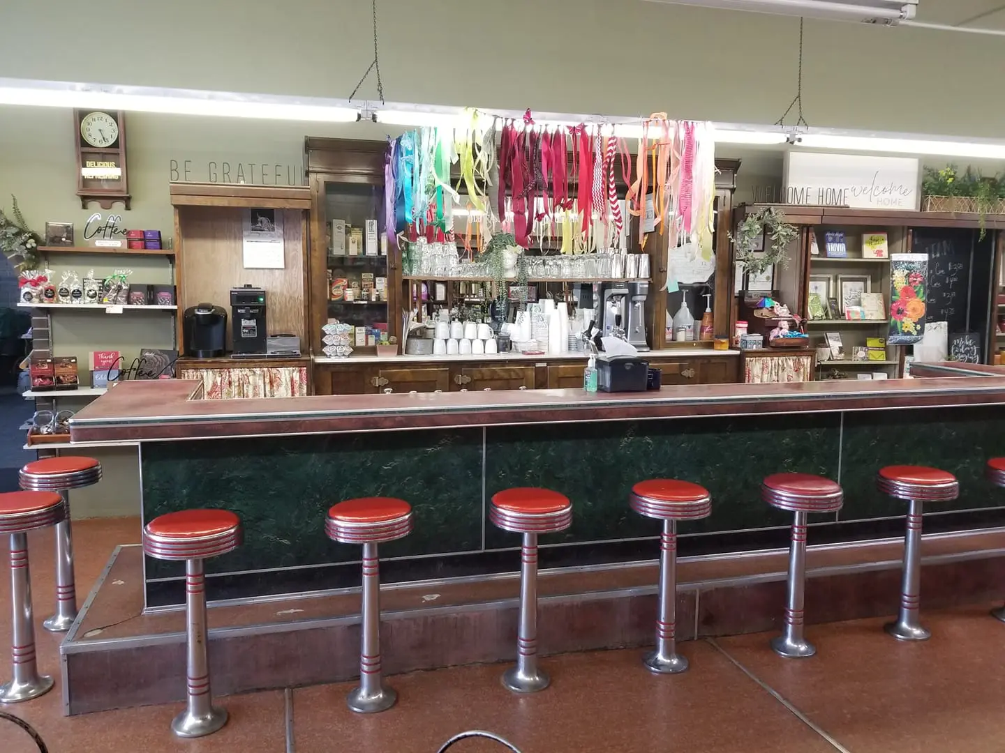 Standing behind an old soda fountain with a red counter, red stools and a colorful array of ribbons hanging from the ceiling.