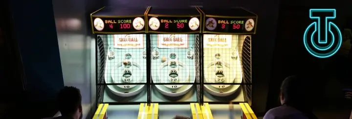 Three skee ball machines glow in a dark room.