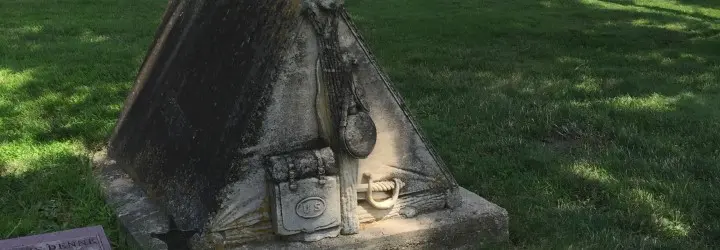 A tombstone carved in the shape of a pup tent sits among plain headstones.
