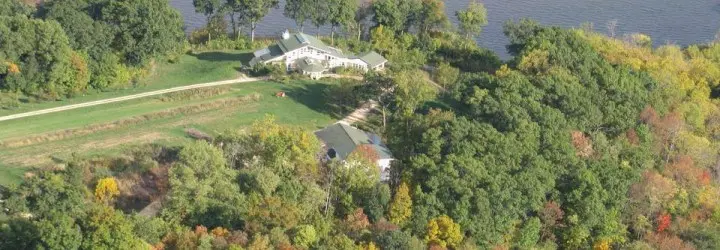 A large building sits atop a river bluff surrounded by fall-colored trees.