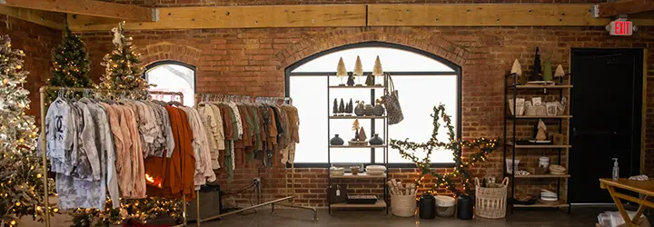 A clothing rack and other sale displays sit among holiday decorations in front of a historic brick wall.