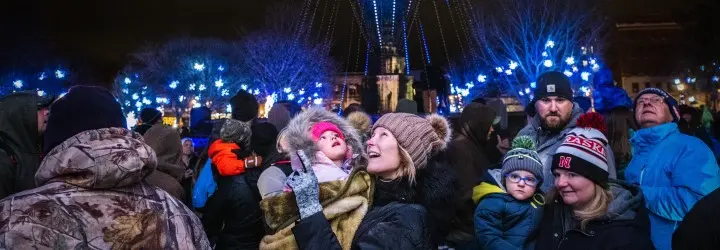 A white mother holds her child as they gaze up at a vibrant blue holiday light display.