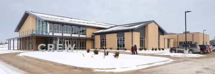 A grand brick building with large class windows and a snow-covered driveway.